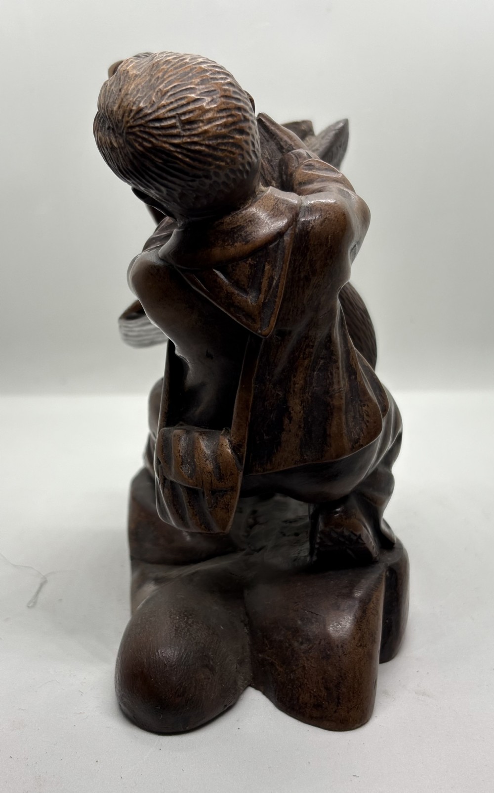 A hand-carved dark wood sculpture depicting a boy sitting alongside a large bird with detailed wing carving. View VI