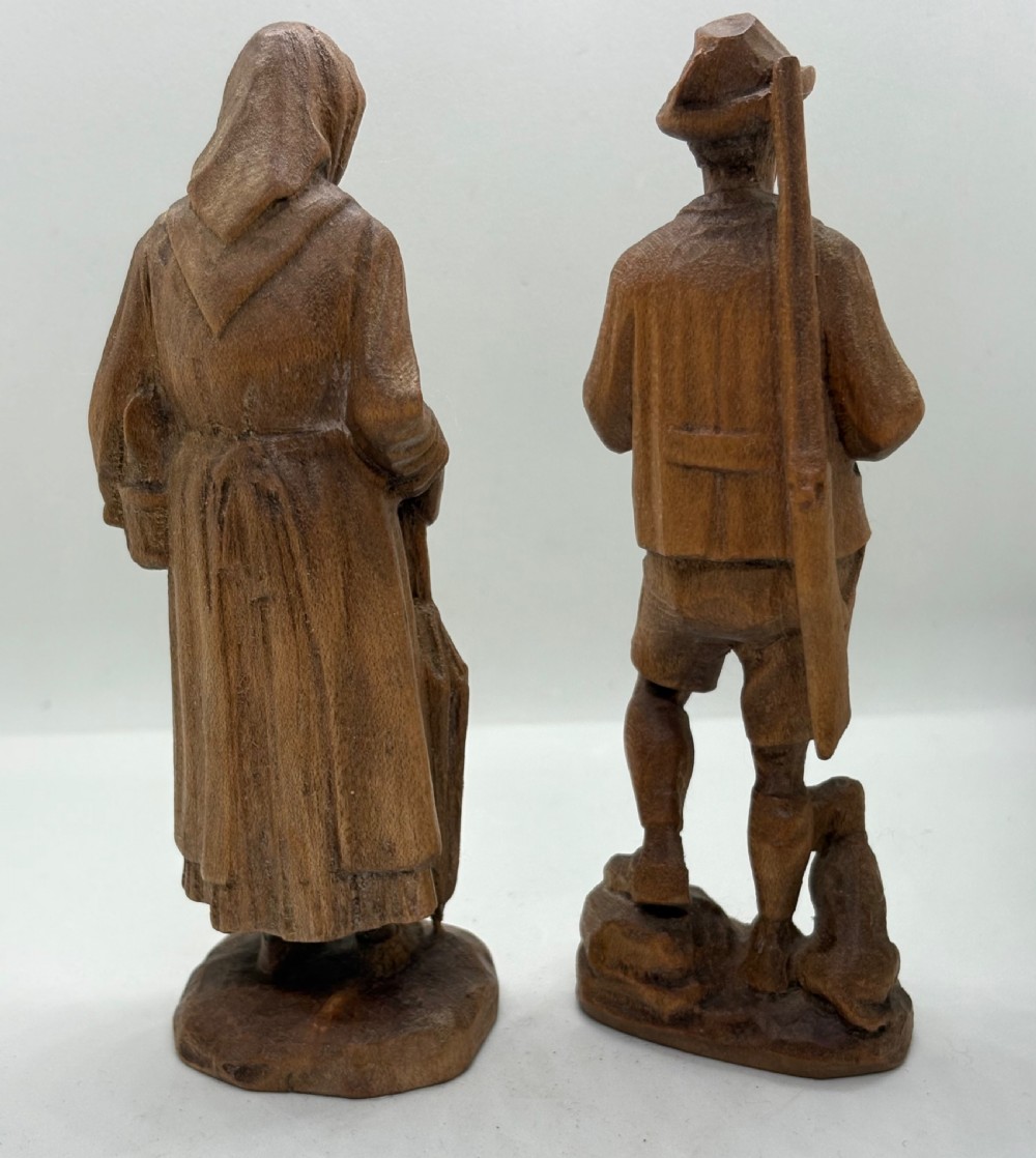 A pair of hand-carved wooden figurines depicting a man smoking a pipe with a small dog alongside a woman holding a basket and umbrella. View II