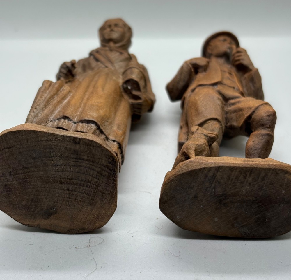 A pair of hand-carved wooden figurines depicting a man smoking a pipe with a small dog alongside a woman holding a basket and umbrella. View III