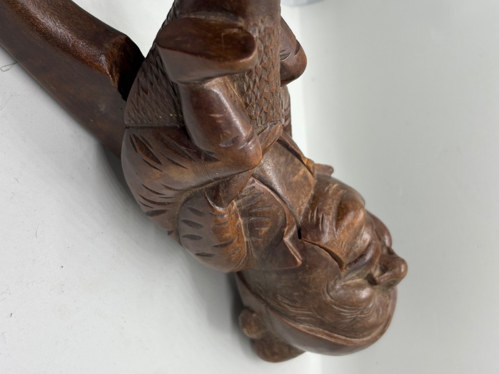A hand-carved dark brown wood Black Forest nutcracker in the form of a seated figure with an integrated lever mechanism. View III