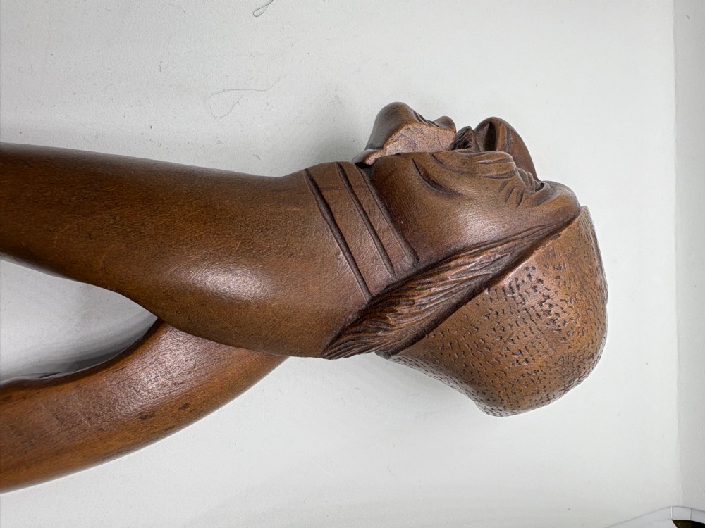 A hand-carved dark wood nutcracker shaped as a man wearing a cap with a lever mechanism forming his jaw. View II