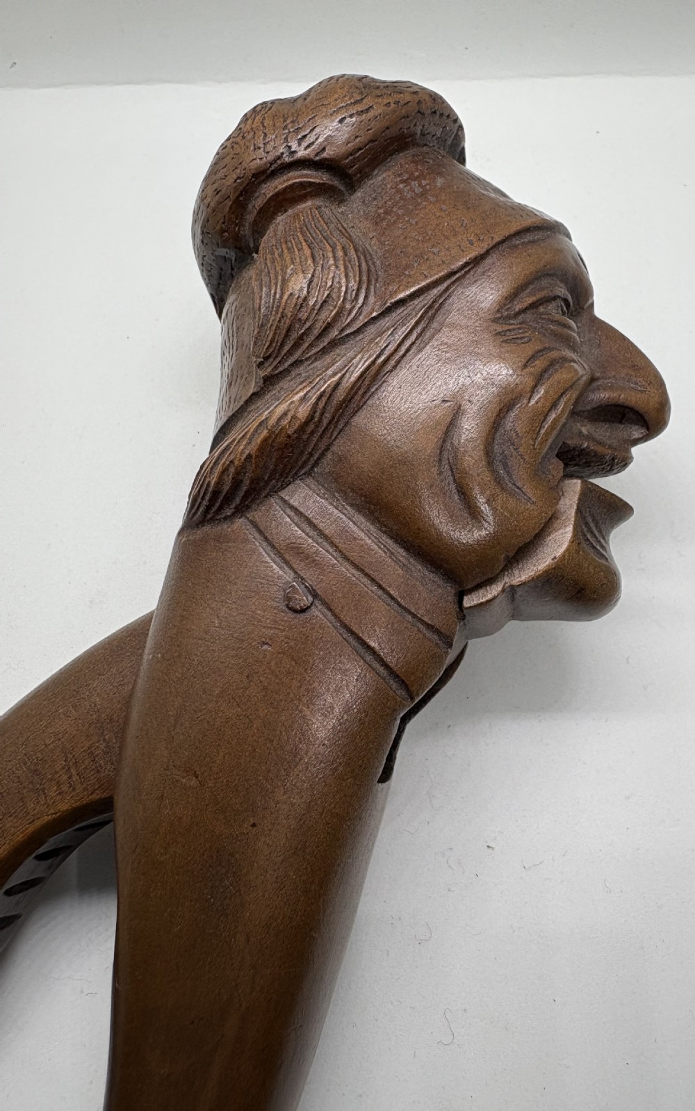 A hand-carved dark wood nutcracker shaped as a man wearing a cap with a lever mechanism forming his jaw. View III