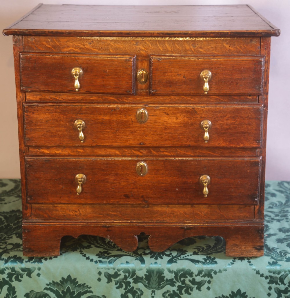 A small Georgian oak chest of drawers featuring brass drop handles, keyhole escutcheons, and a shaped apron with bracket feet.