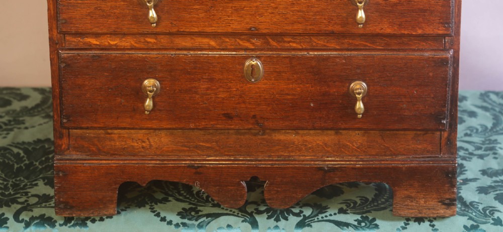A small Georgian oak chest of drawers featuring brass drop handles, keyhole escutcheons, and a shaped apron with bracket feet. View II