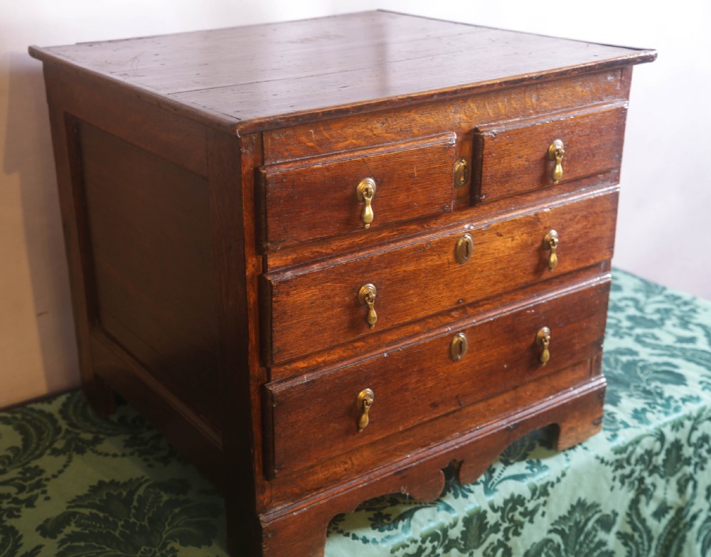 A small Georgian oak chest of drawers featuring brass drop handles, keyhole escutcheons, and a shaped apron with bracket feet. View III