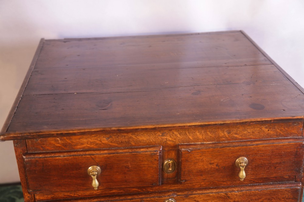 A small Georgian oak chest of drawers featuring brass drop handles, keyhole escutcheons, and a shaped apron with bracket feet. View V