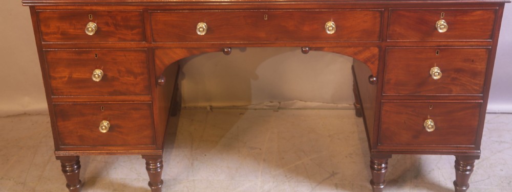 A 19th-century mahogany kneehole desk featuring multiple drawers with brass knobs, a central arched apron, and turned legs. View II