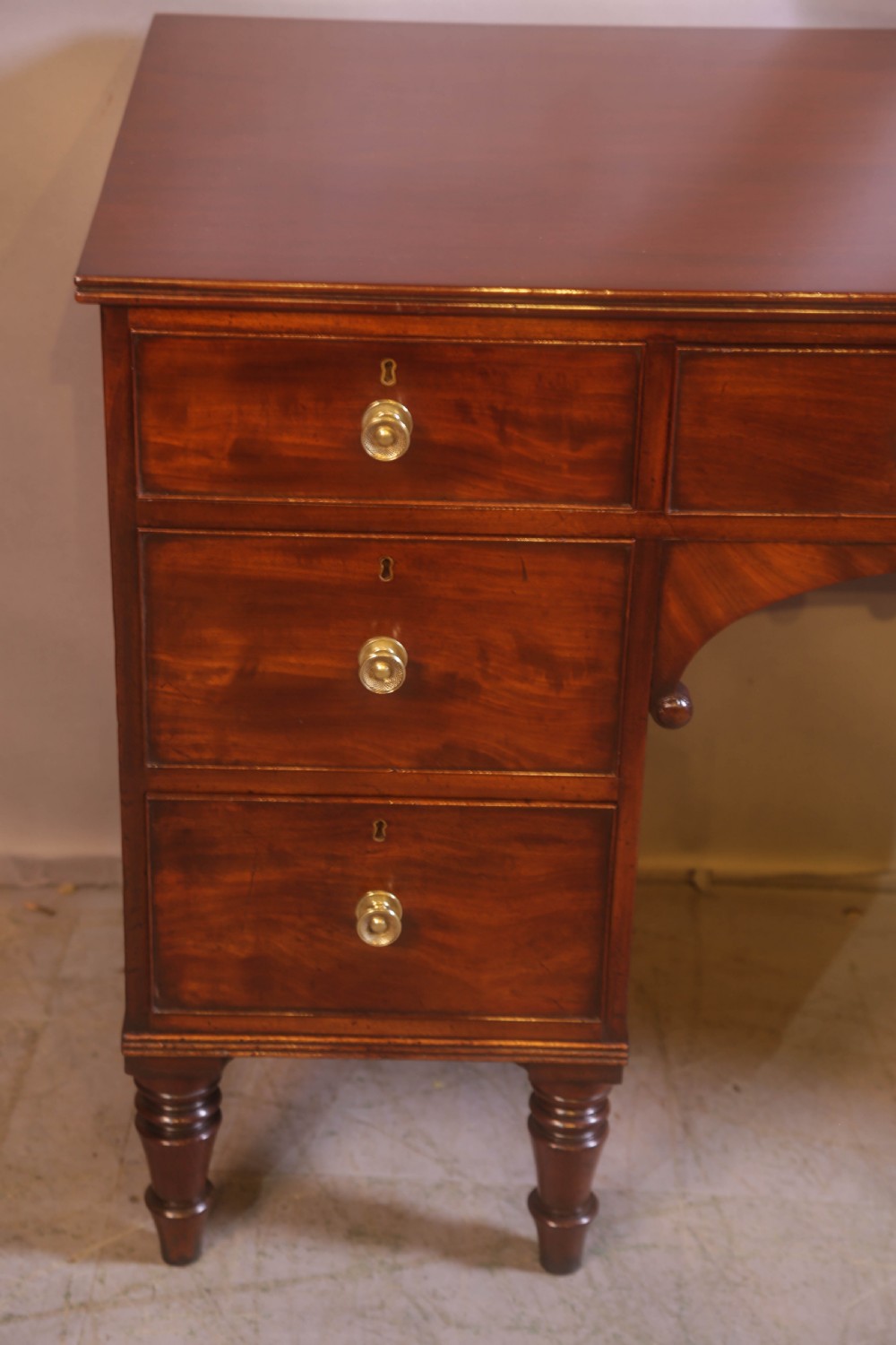 A 19th-century mahogany kneehole desk featuring multiple drawers with brass knobs, a central arched apron, and turned legs. View III