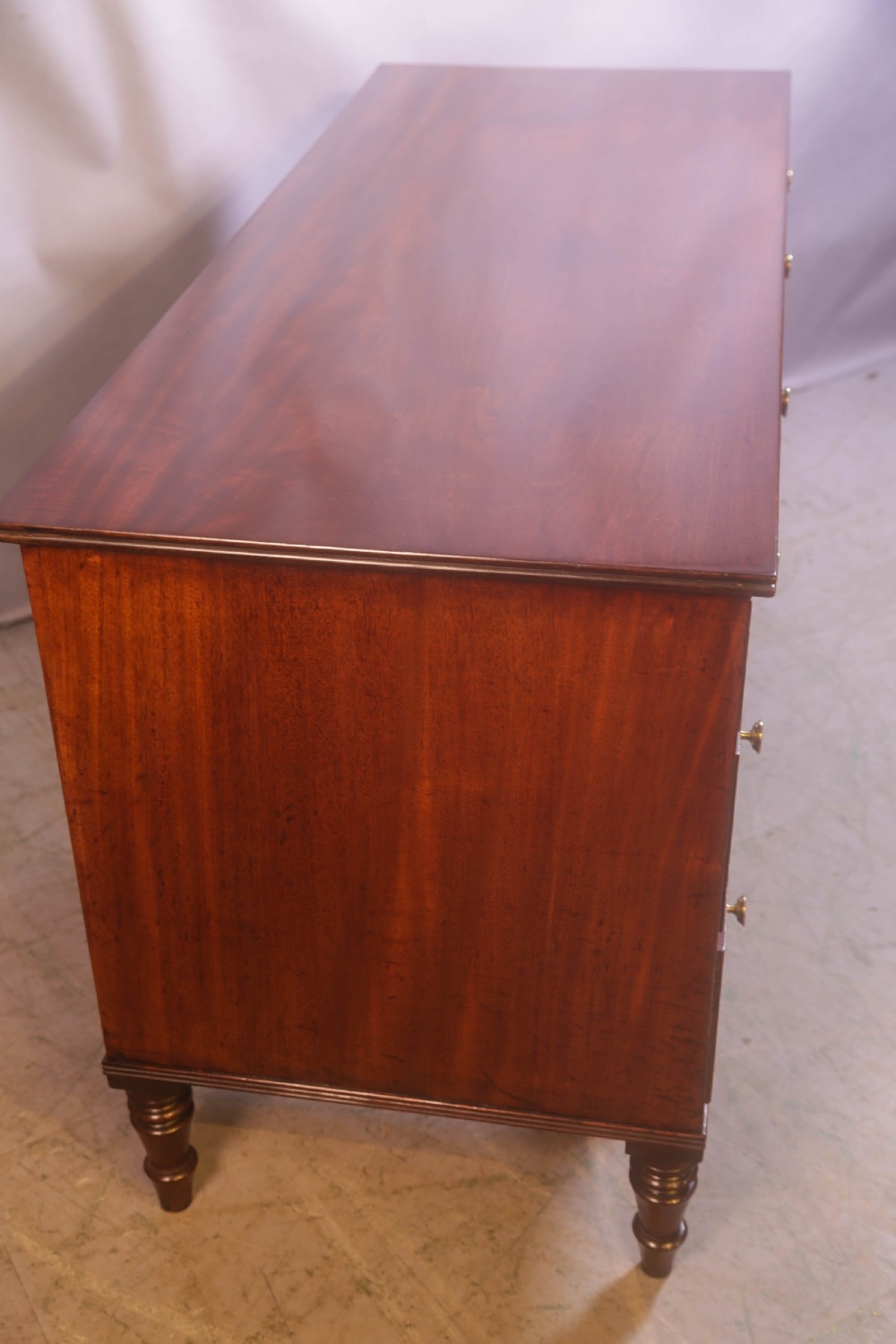 A 19th-century mahogany kneehole desk featuring multiple drawers with brass knobs, a central arched apron, and turned legs. View V