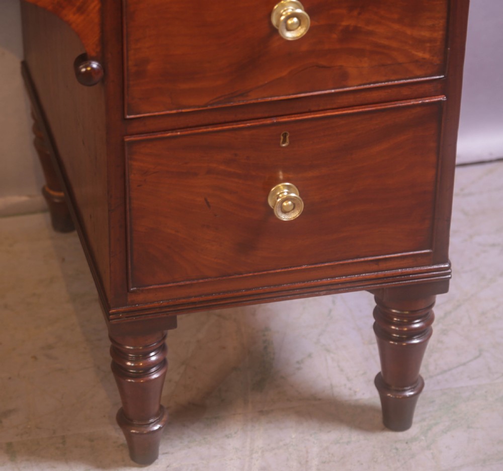 A 19th-century mahogany kneehole desk featuring multiple drawers with brass knobs, a central arched apron, and turned legs. View VII