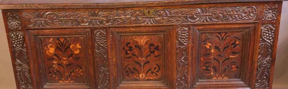 An antique carved oak coffer featuring three floral inlaid panels, carved frieze work, and two lower drawers with brass handles. View II