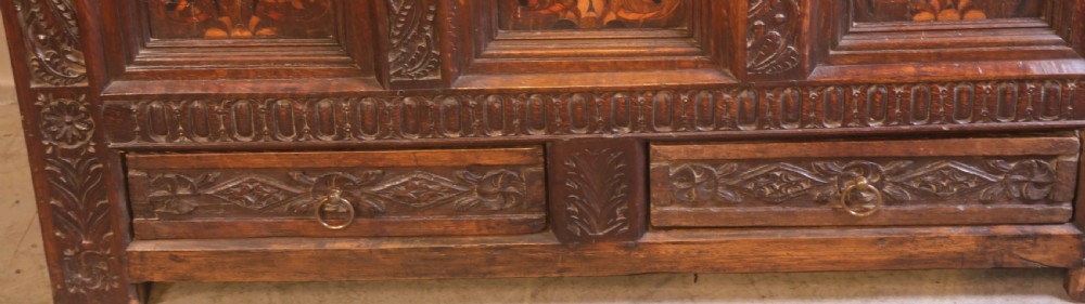 An antique carved oak coffer featuring three floral inlaid panels, carved frieze work, and two lower drawers with brass handles. View III