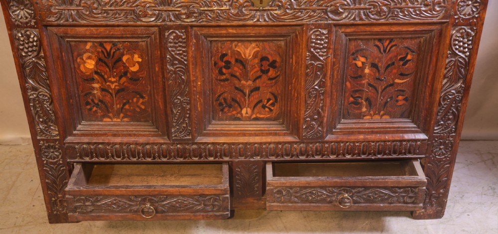 An antique carved oak coffer featuring three floral inlaid panels, carved frieze work, and two lower drawers with brass handles. View IV