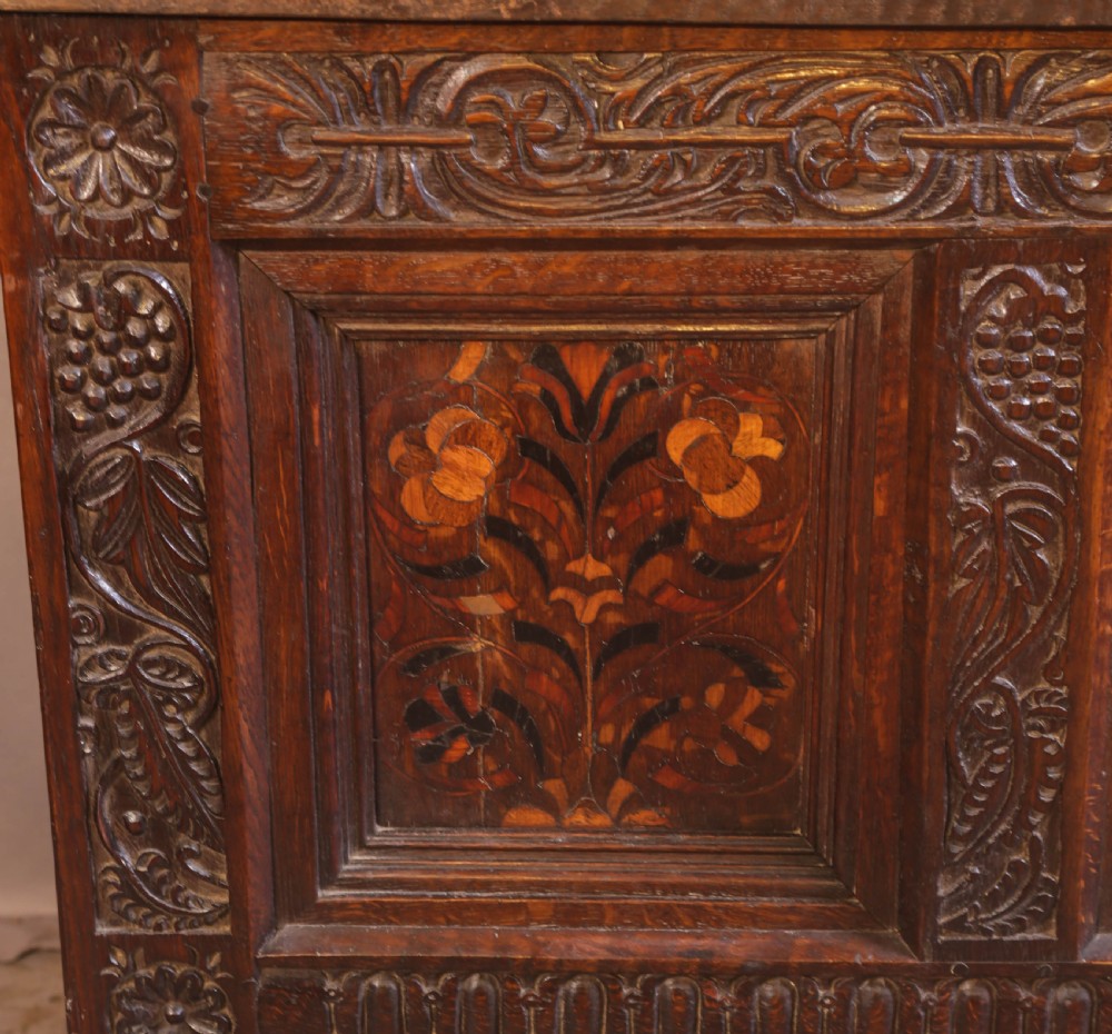 An antique carved oak coffer featuring three floral inlaid panels, carved frieze work, and two lower drawers with brass handles. View VI