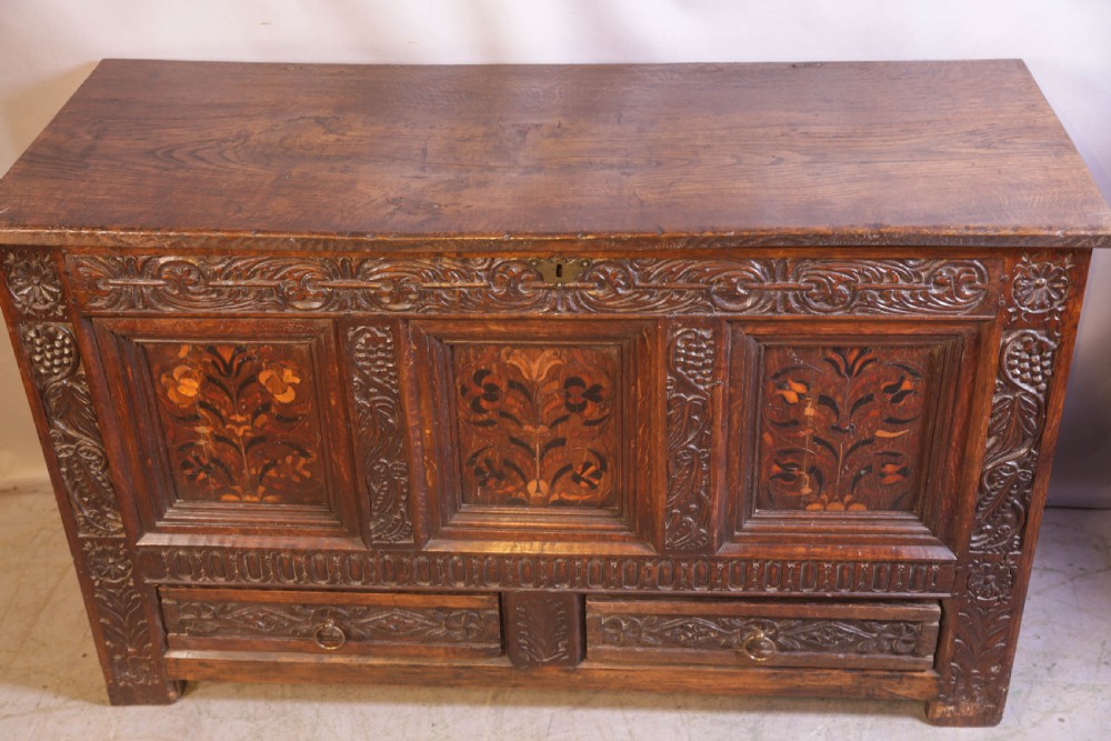 An antique carved oak coffer featuring three floral inlaid panels, carved frieze work, and two lower drawers with brass handles. View XI