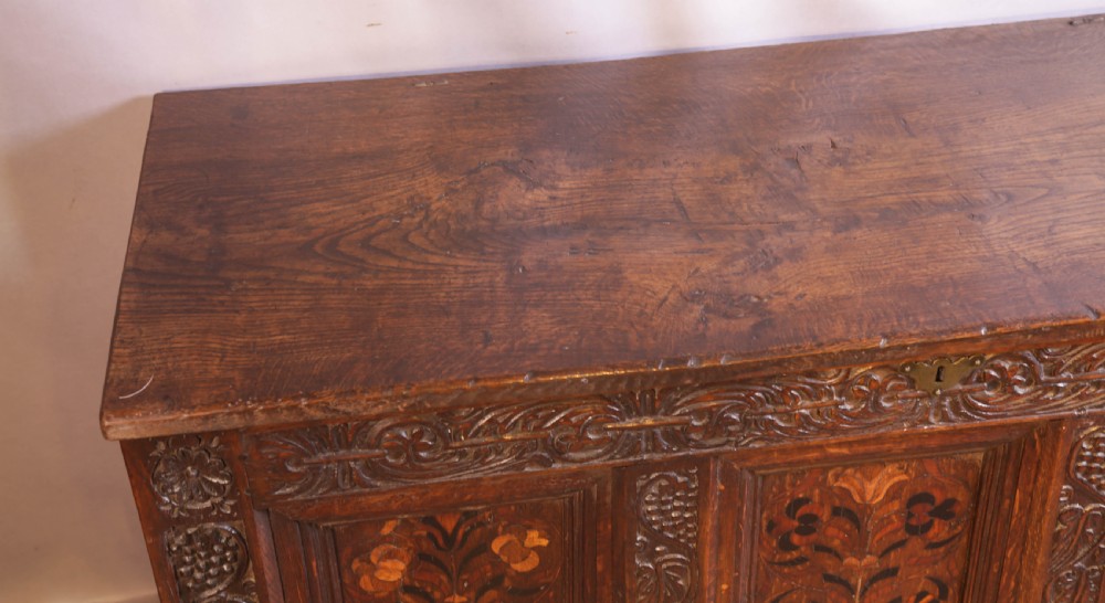 An antique carved oak coffer featuring three floral inlaid panels, carved frieze work, and two lower drawers with brass handles. View XII
