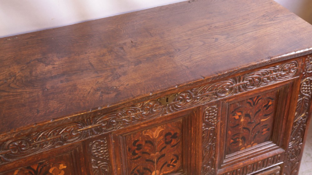 An antique carved oak coffer featuring three floral inlaid panels, carved frieze work, and two lower drawers with brass handles. View XIII