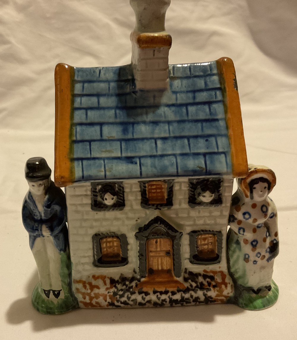 A Regency Prattware earthenware cottage figure featuring a blue tiled roof, central chimney, and relief figures standing on either side.