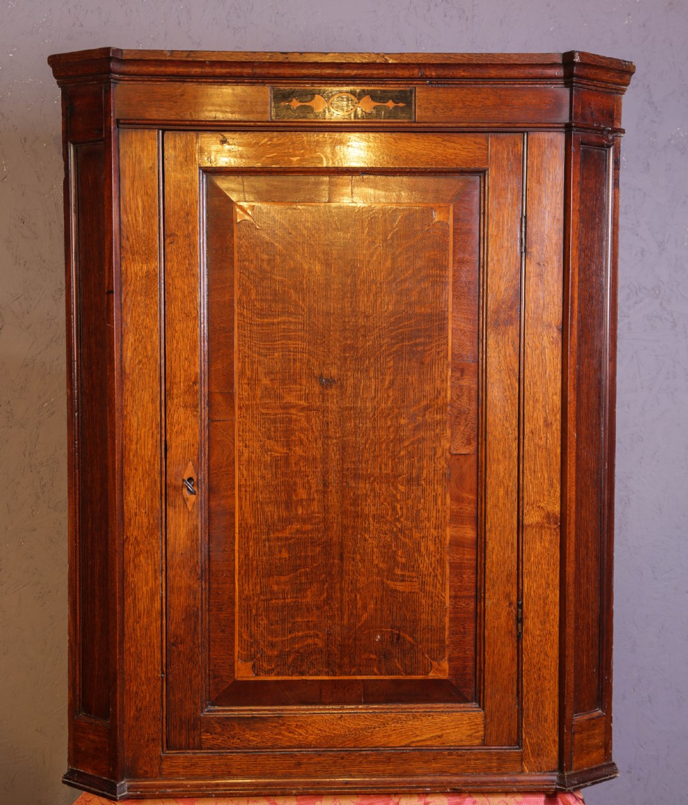 An eighteenth-century oak corner cupboard featuring a single panelled door with crossbanded inlay, a top marquetry motif, and a diamond keyhole.