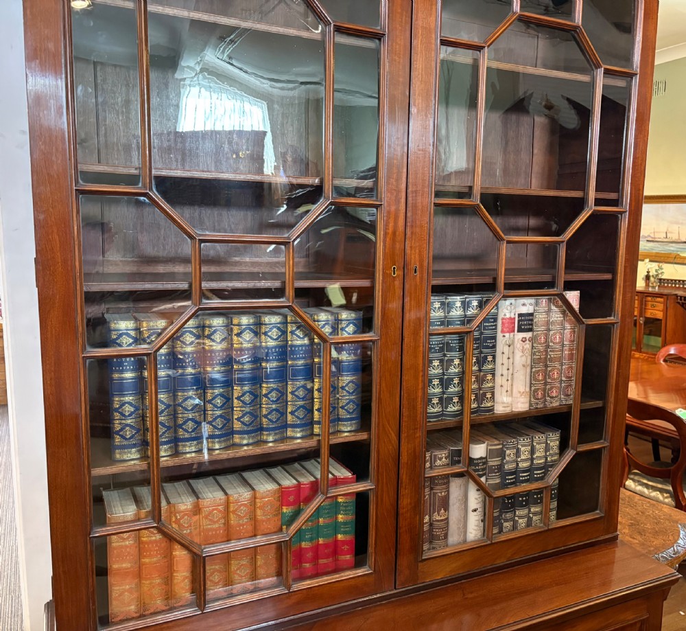 A Georgian mahogany library bookcase featuring a broken swan-neck pediment with a central gilded urn finial, two astragal glazed upper doors, and two solid panelled cabinet doors below. View V