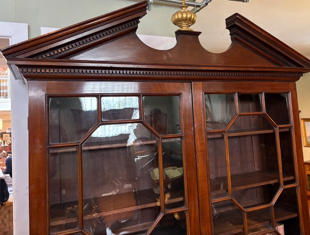 A Georgian mahogany library bookcase featuring a broken swan-neck pediment with a central gilded urn finial, two astragal glazed upper doors, and two solid panelled cabinet doors below. View VII
