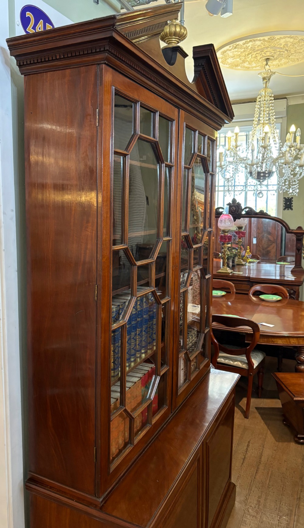 A Georgian mahogany library bookcase featuring a broken swan-neck pediment with a central gilded urn finial, two astragal glazed upper doors, and two solid panelled cabinet doors below. View XI