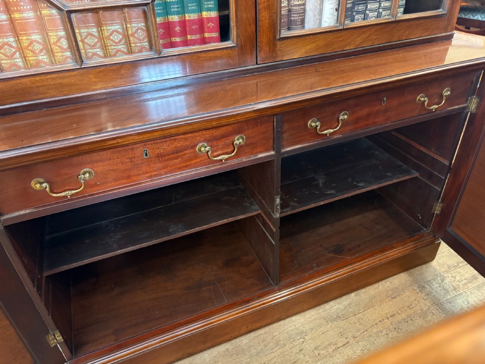 A Georgian mahogany library bookcase featuring a broken swan-neck pediment with a central gilded urn finial, two astragal glazed upper doors, and two solid panelled cabinet doors below. View XVI