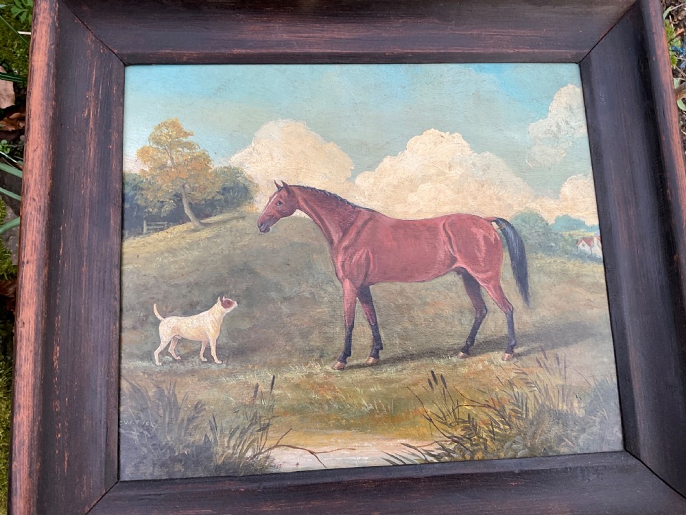 An antique oil painting depicting a chestnut horse standing alongside a small white terrier in a grassy landscape within a dark wooden frame.