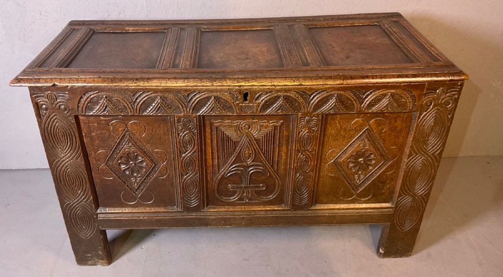 A seventeenth-century dark oak coffer featuring a framed panel lid and three front panels carved with geometric lozenge patterns.