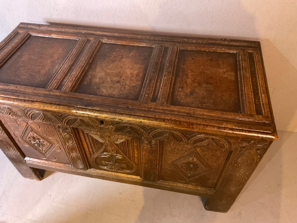 A seventeenth-century dark oak coffer featuring a framed panel lid and three front panels carved with geometric lozenge patterns. View IX