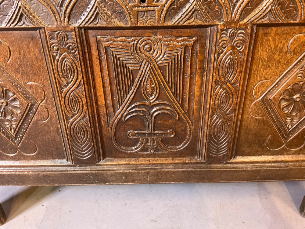 A seventeenth-century dark oak coffer featuring a framed panel lid and three front panels carved with geometric lozenge patterns. View X