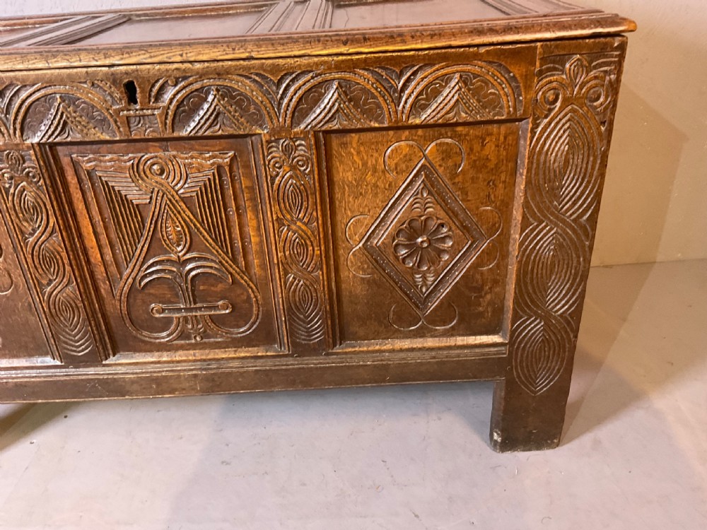 A seventeenth-century dark oak coffer featuring a framed panel lid and three front panels carved with geometric lozenge patterns. View XI