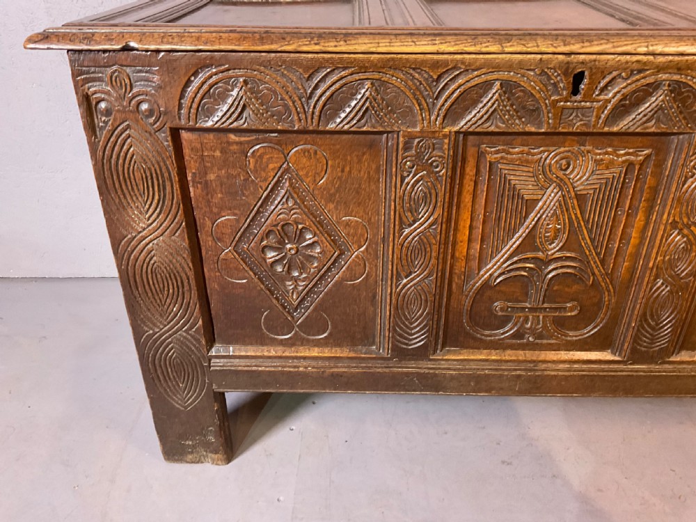 A seventeenth-century dark oak coffer featuring a framed panel lid and three front panels carved with geometric lozenge patterns. View XII