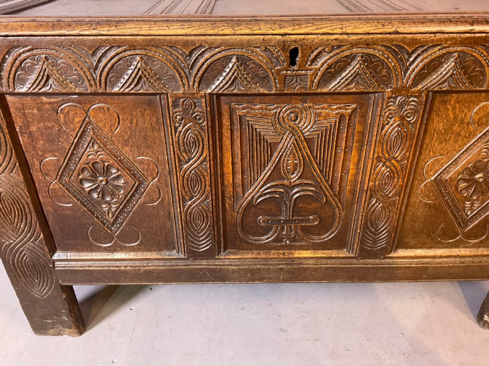 A seventeenth-century dark oak coffer featuring a framed panel lid and three front panels carved with geometric lozenge patterns. View XIII