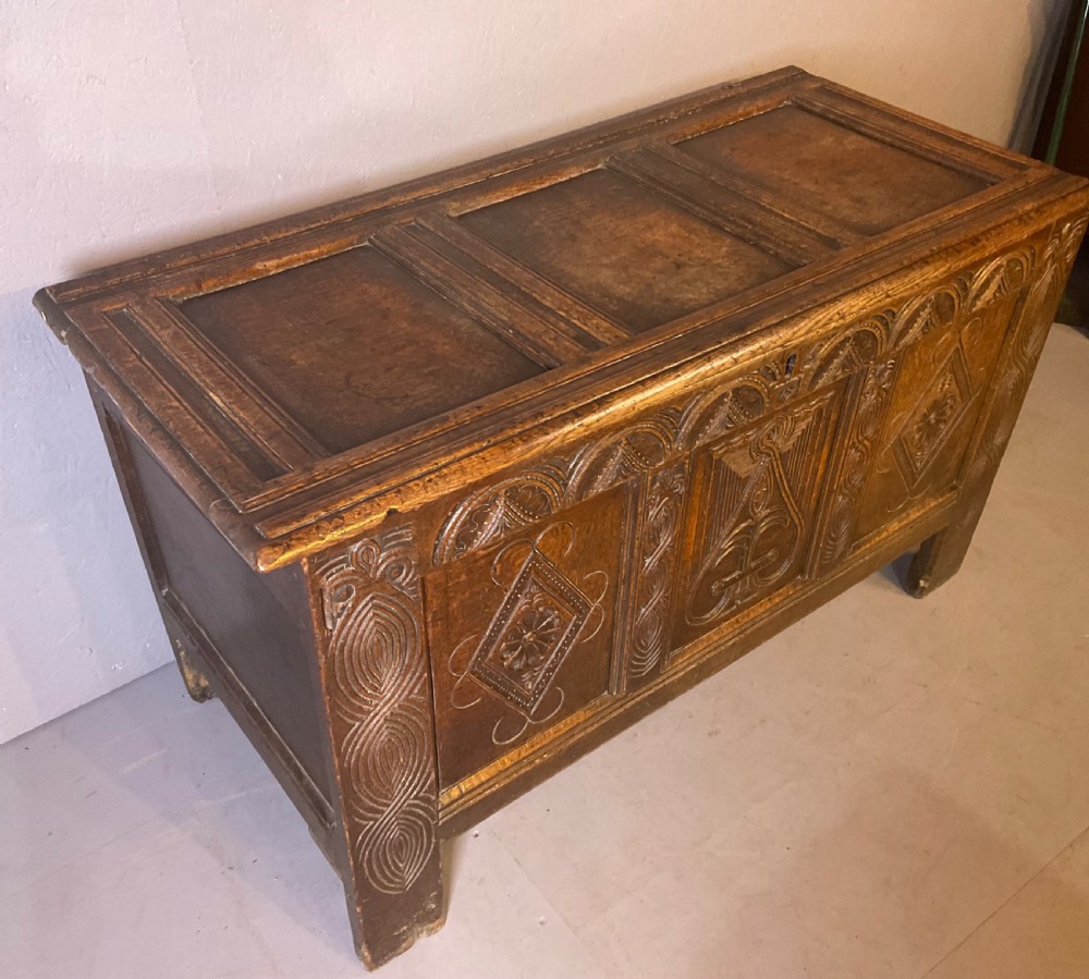A seventeenth-century dark oak coffer featuring a framed panel lid and three front panels carved with geometric lozenge patterns. View XIV