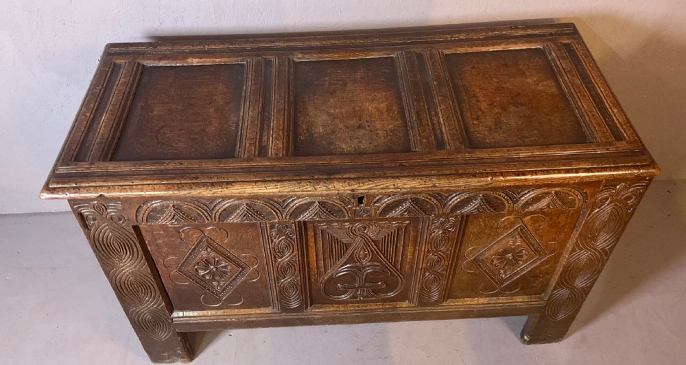 A seventeenth-century dark oak coffer featuring a framed panel lid and three front panels carved with geometric lozenge patterns. View XX