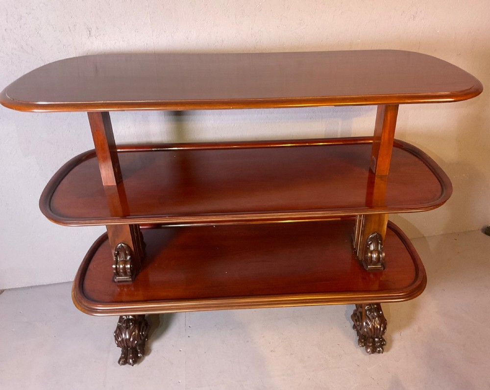 A Victorian three-tiered mahogany metamorphic dumb waiter featuring rounded shelf edges and carved scroll feet.