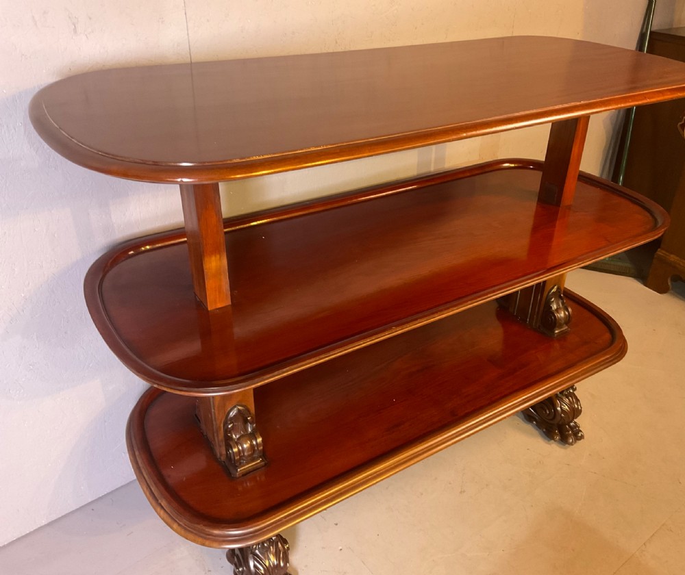A Victorian three-tiered mahogany metamorphic dumb waiter featuring rounded shelf edges and carved scroll feet. View II
