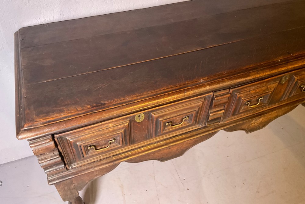 A late seventeenth-century dark oak serving dresser featuring three geometric moulded drawers with brass handles and a scalloped lower apron set on turned legs. View IV