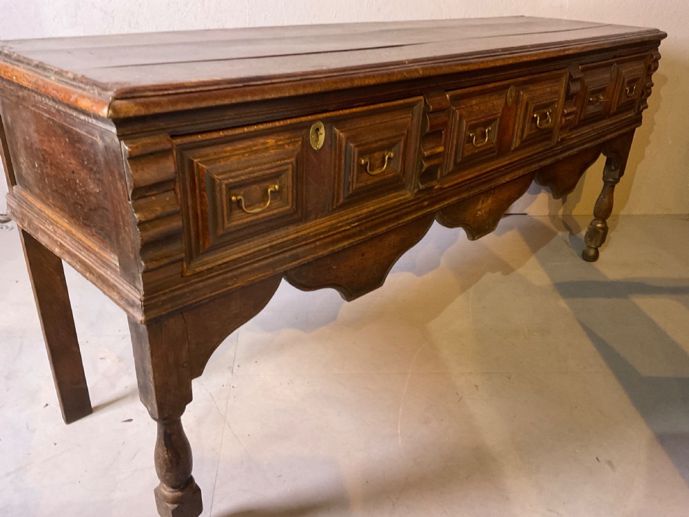 A late seventeenth-century dark oak serving dresser featuring three geometric moulded drawers with brass handles and a scalloped lower apron set on turned legs. View XI