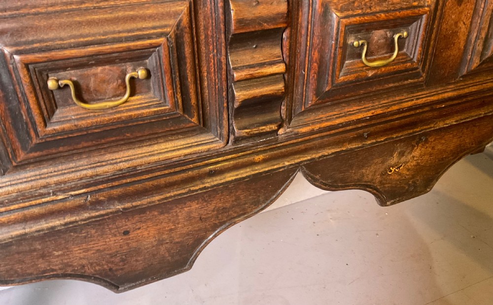 A late seventeenth-century dark oak serving dresser featuring three geometric moulded drawers with brass handles and a scalloped lower apron set on turned legs. View XV