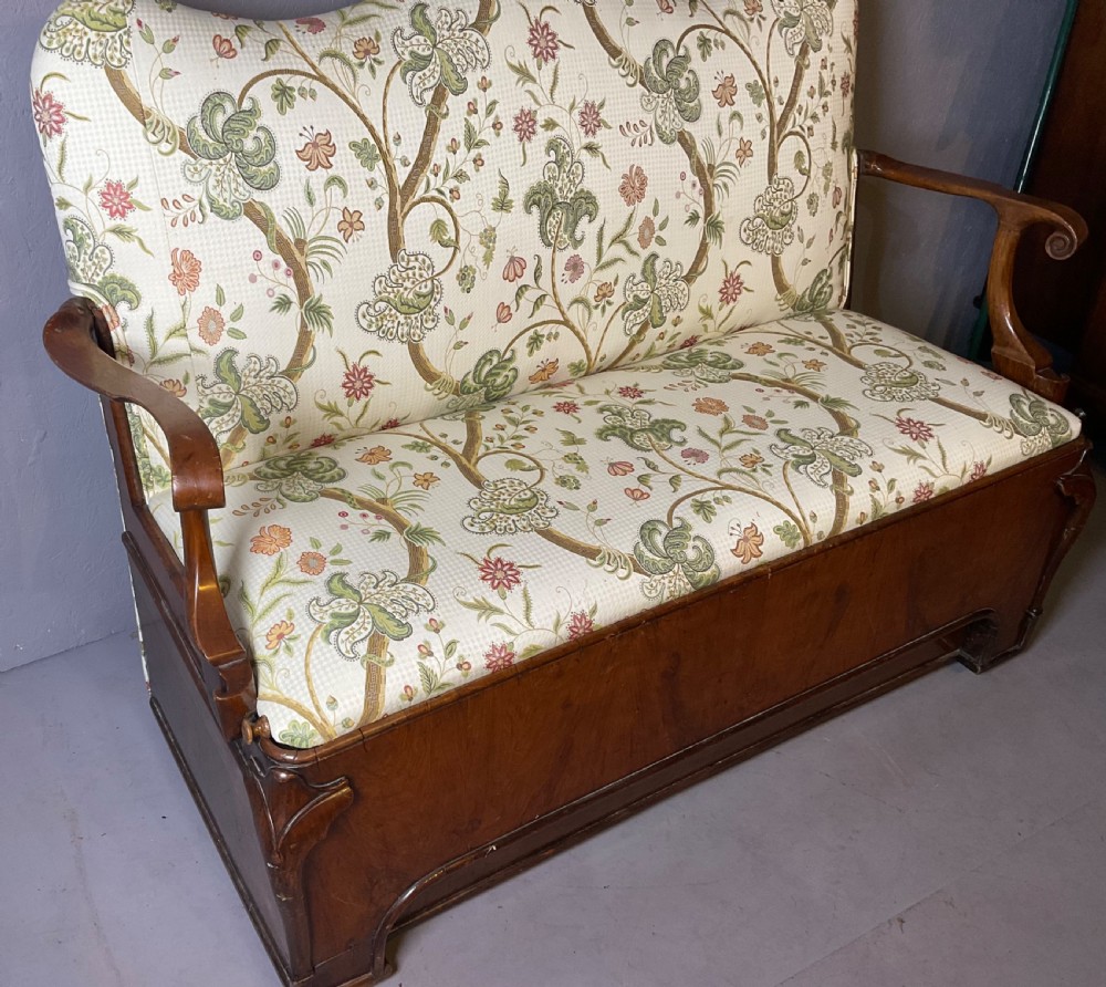 A Queen Anne style walnut settee featuring contoured wooden arms, a shaped upholstered backrest, and botanical floral pattern fabric. View IV