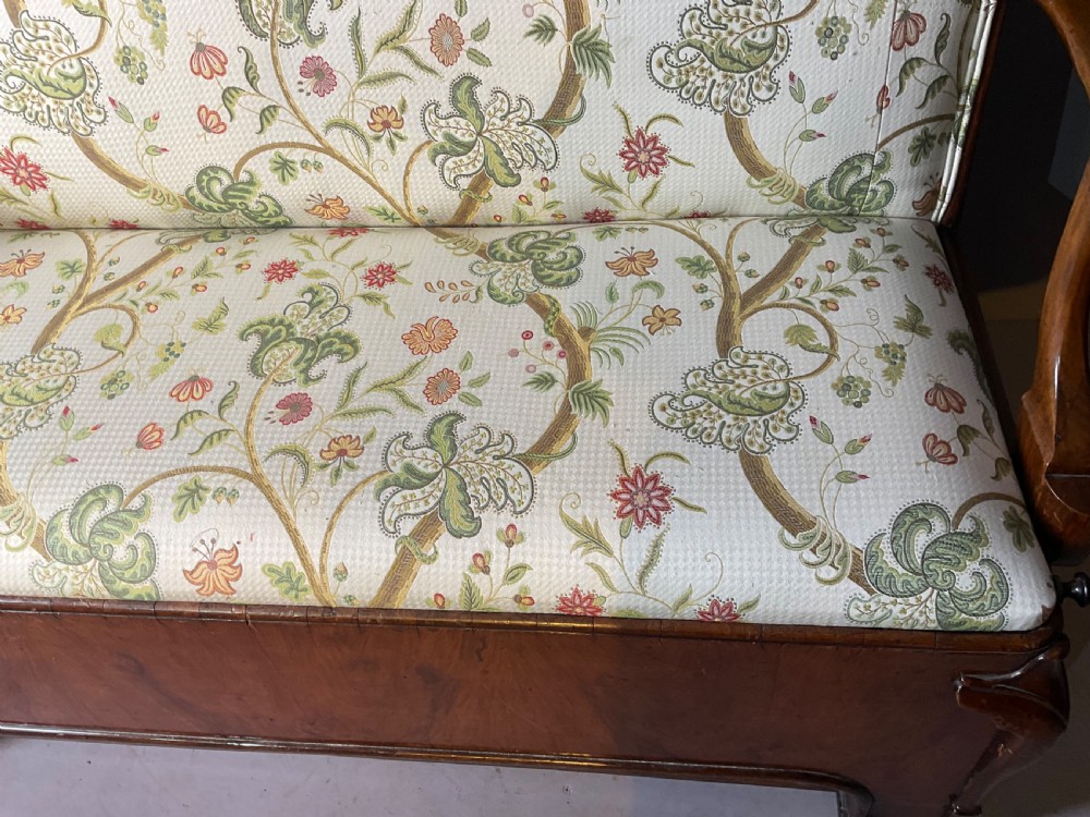A Queen Anne style walnut settee featuring contoured wooden arms, a shaped upholstered backrest, and botanical floral pattern fabric. View V