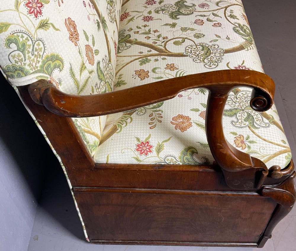 A Queen Anne style walnut settee featuring contoured wooden arms, a shaped upholstered backrest, and botanical floral pattern fabric. View VII
