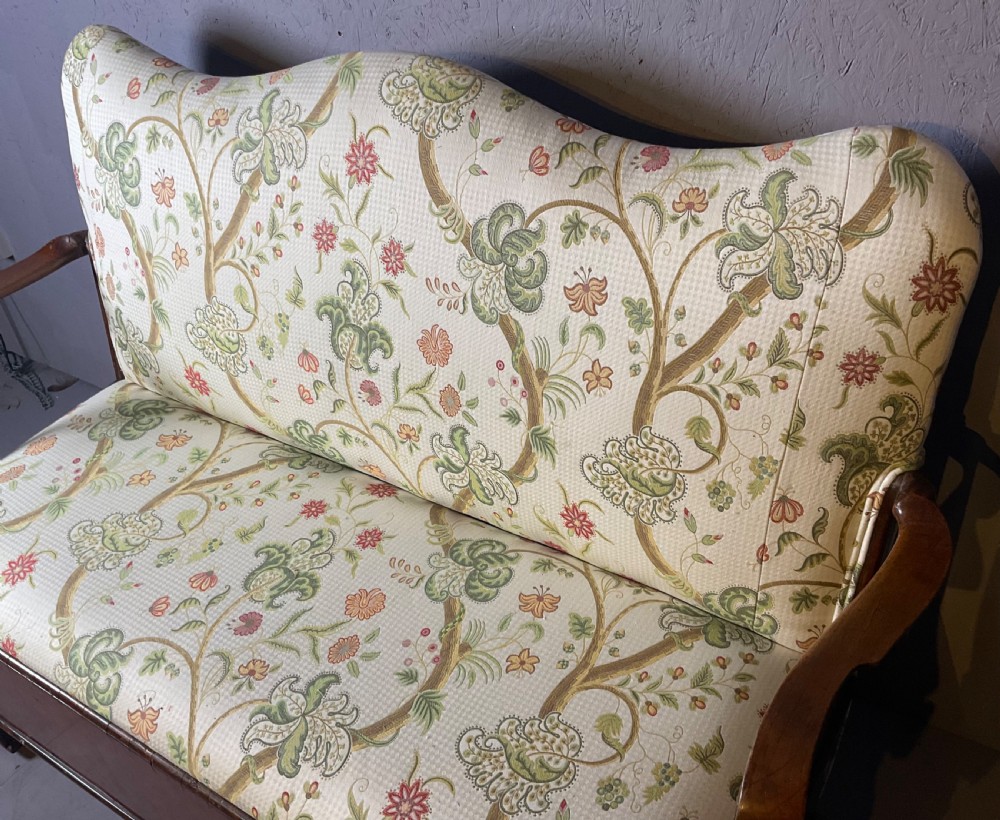 A Queen Anne style walnut settee featuring contoured wooden arms, a shaped upholstered backrest, and botanical floral pattern fabric. View X