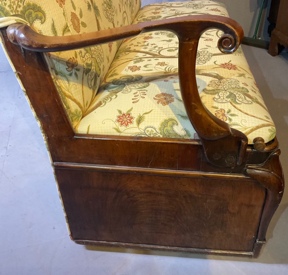 A Queen Anne style walnut settee featuring contoured wooden arms, a shaped upholstered backrest, and botanical floral pattern fabric. View XV