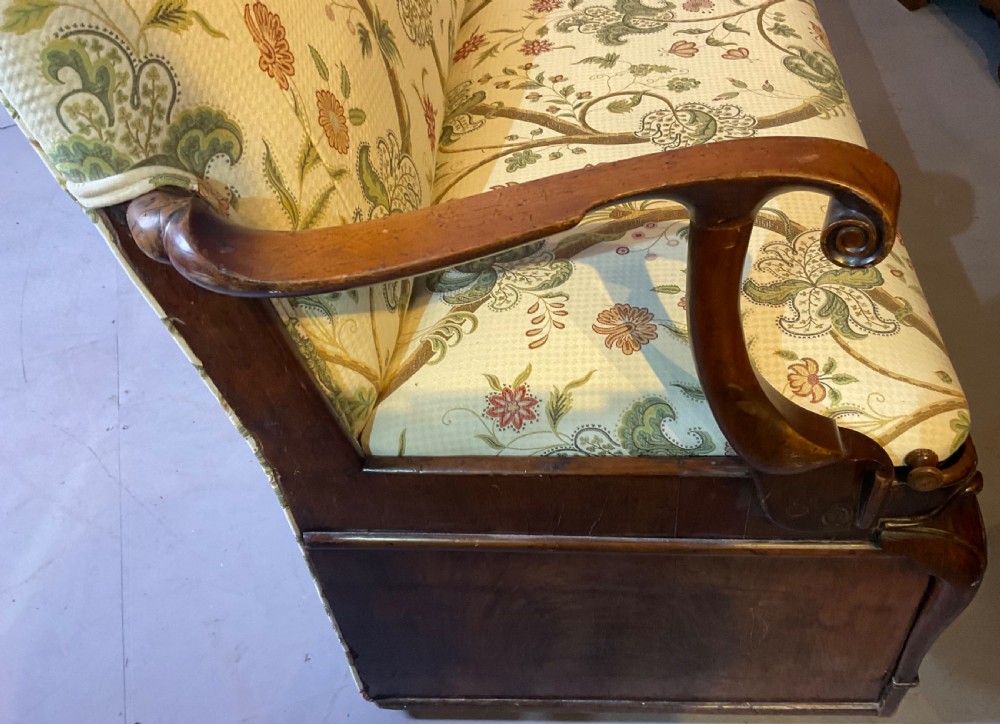 A Queen Anne style walnut settee featuring contoured wooden arms, a shaped upholstered backrest, and botanical floral pattern fabric. View XVI