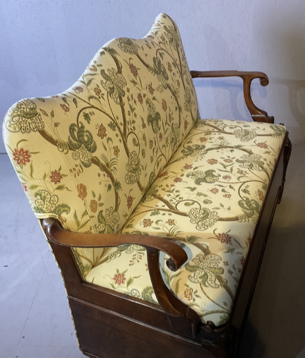 A Queen Anne style walnut settee featuring contoured wooden arms, a shaped upholstered backrest, and botanical floral pattern fabric. View XVII