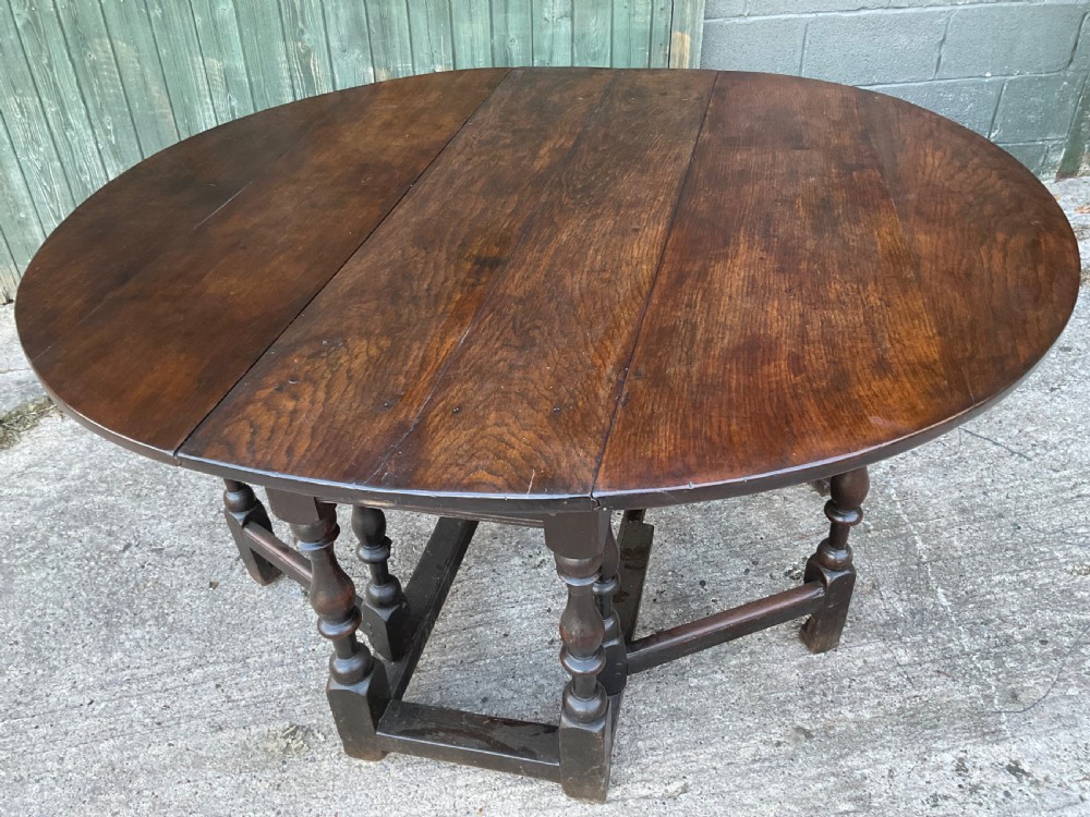 Underside view of a dark brown oak gateleg table showing baluster turned legs, stretchers, hand-forged iron hinges, and hinged drop leaves. View II