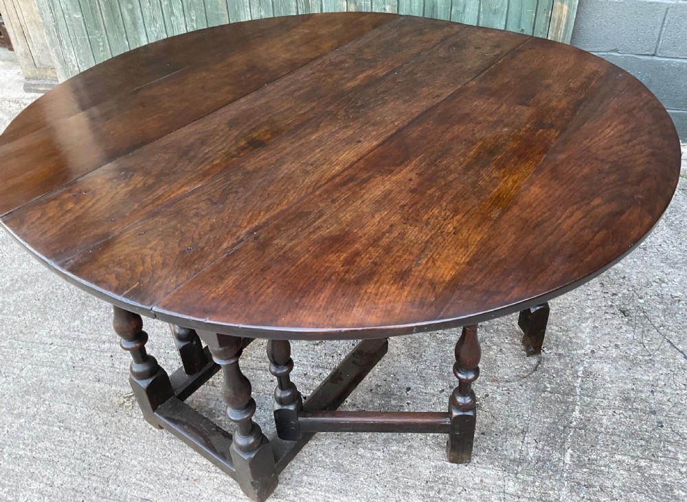 Underside view of a dark brown oak gateleg table showing baluster turned legs, stretchers, hand-forged iron hinges, and hinged drop leaves. View IV